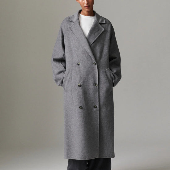 Person wearing a long gray coat against a plain background