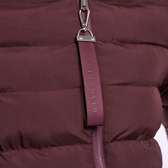 Close-up of a quilted puffer jacket in a deep plum-burgundy color, featuring a silver-tone zipper and a matching fabric pull tab with the brand name 'BENDADETE' printed vertically.