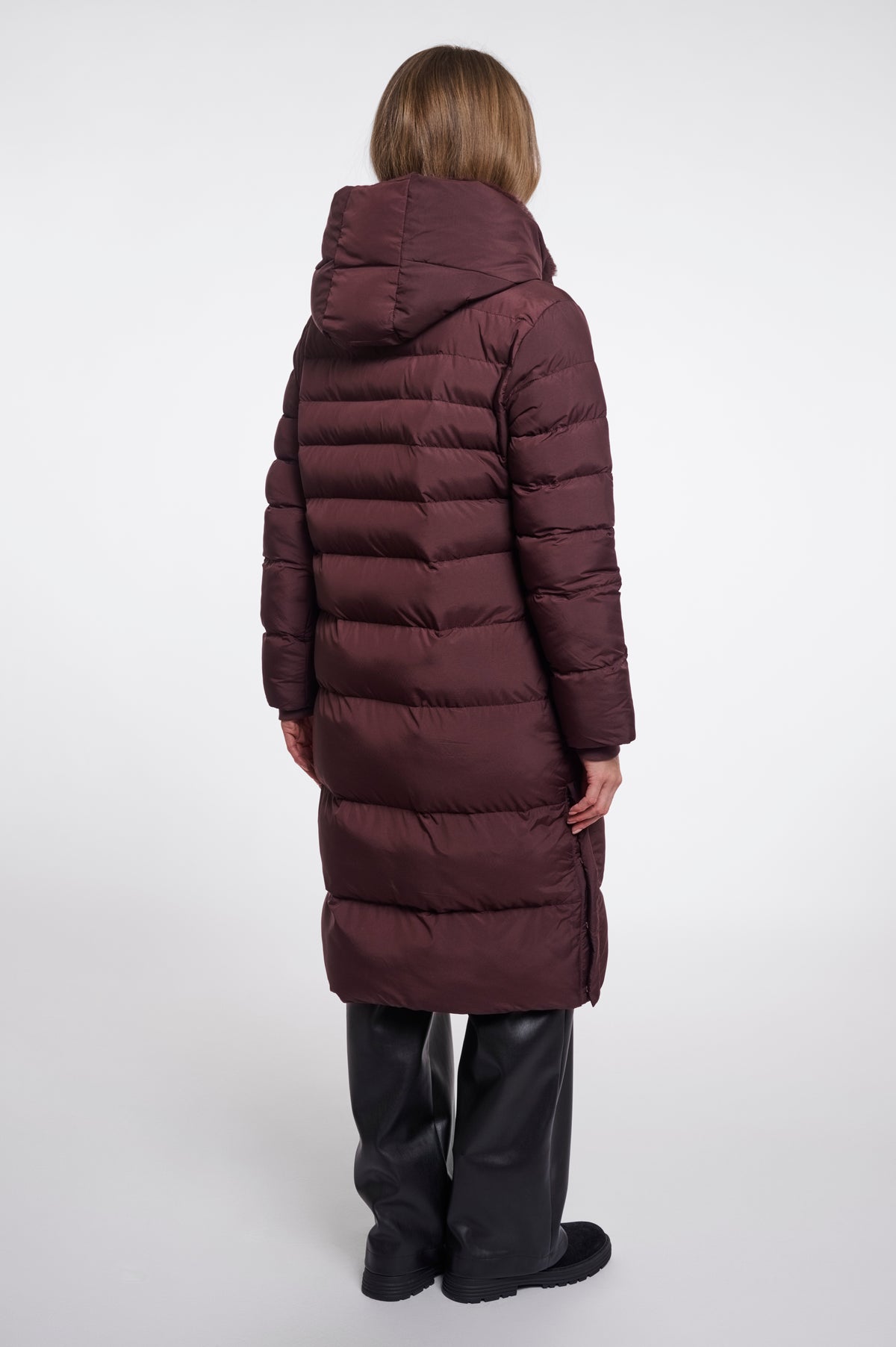Person wearing a long burgundy puffer coat on a white background