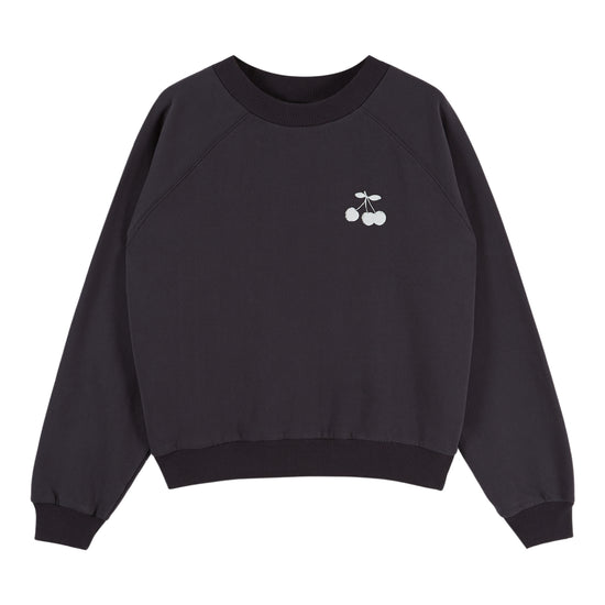 A black crewneck sweatshirt with raglan sleeves, featuring a small white embroidered cherry graphic on the left chest, displayed against a solid white background.