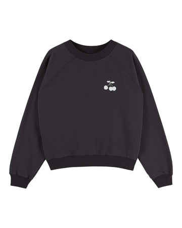 A black crewneck sweatshirt with raglan sleeves, featuring a small white embroidered cherry graphic on the left chest, displayed against a solid white background.