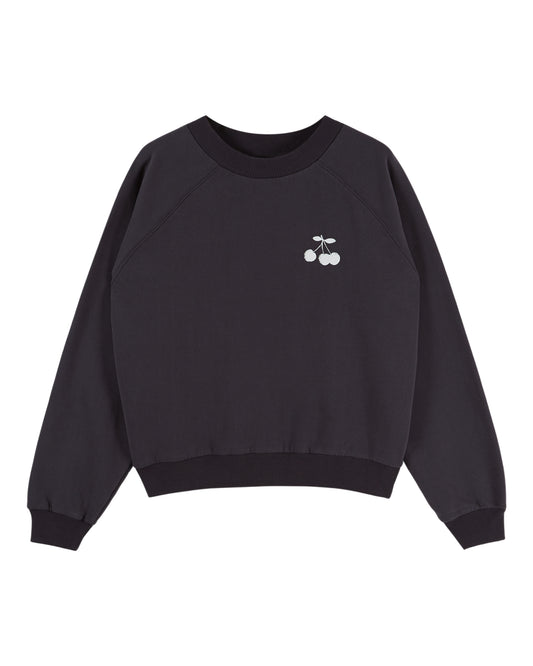 A black crewneck sweatshirt with raglan sleeves, featuring a small white embroidered cherry graphic on the left chest, displayed against a solid white background.