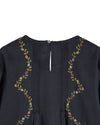 Close-up of the back neckline of a dark navy blue top, featuring vertical pleats down the center, a small button closure, and floral embroidery with green stems and pink, red, and yellow flowers along the shoulders.
