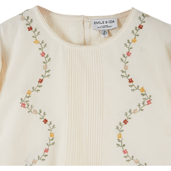 cream blouse with flower embroidery on white background close up of front
