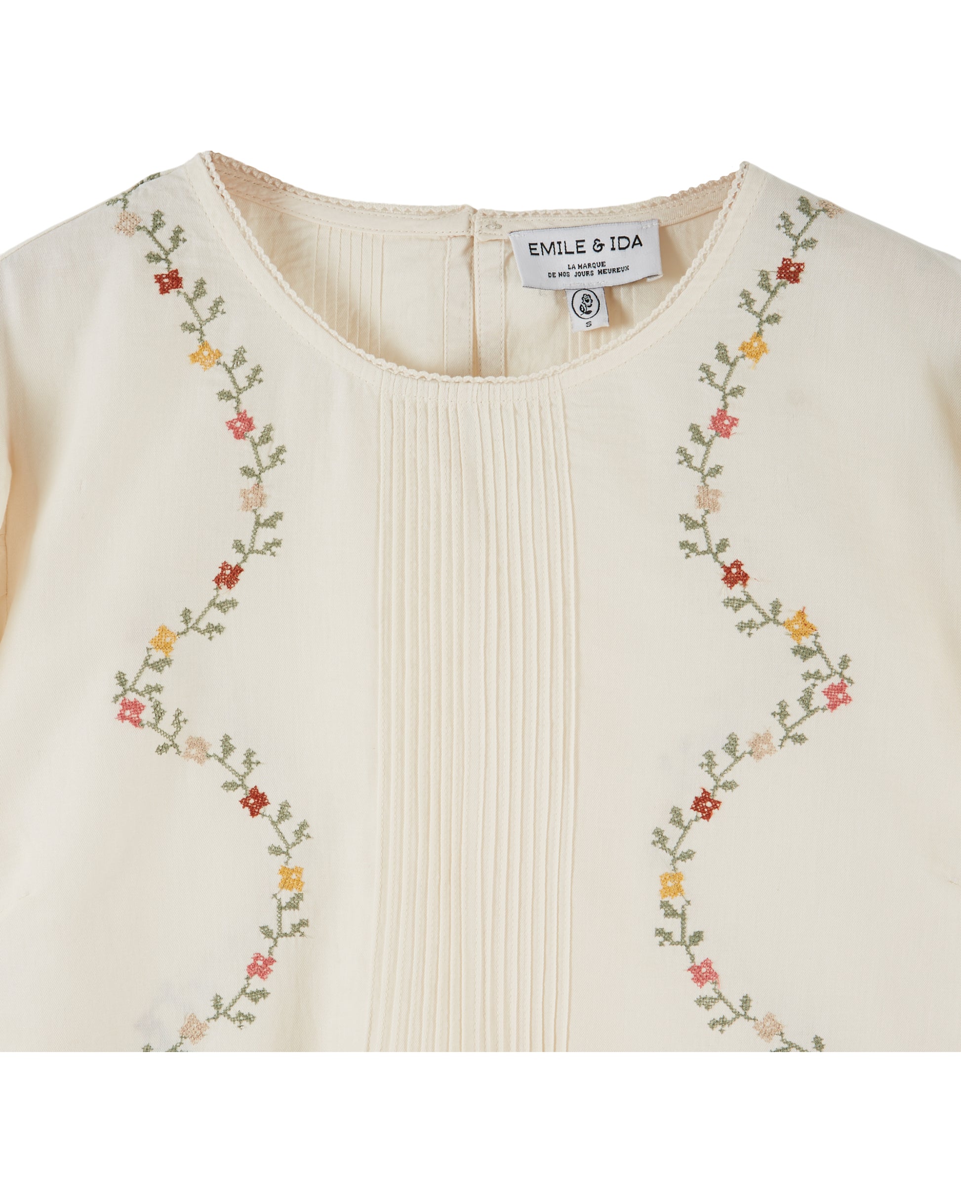 cream blouse with flower embroidery on white background close up of front