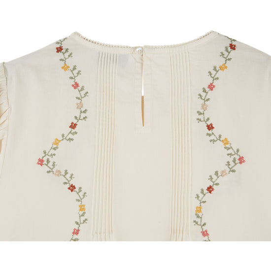 cream blouse with flower embroidery on white background close up of rear view