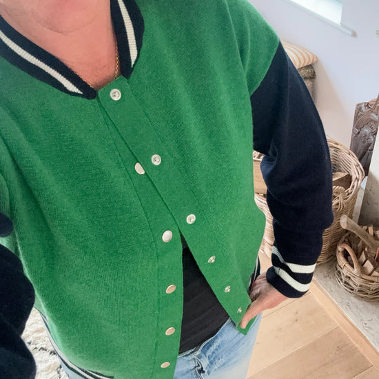 Knitted green bomber jacket with navy sleeves and white details with silver popper closures