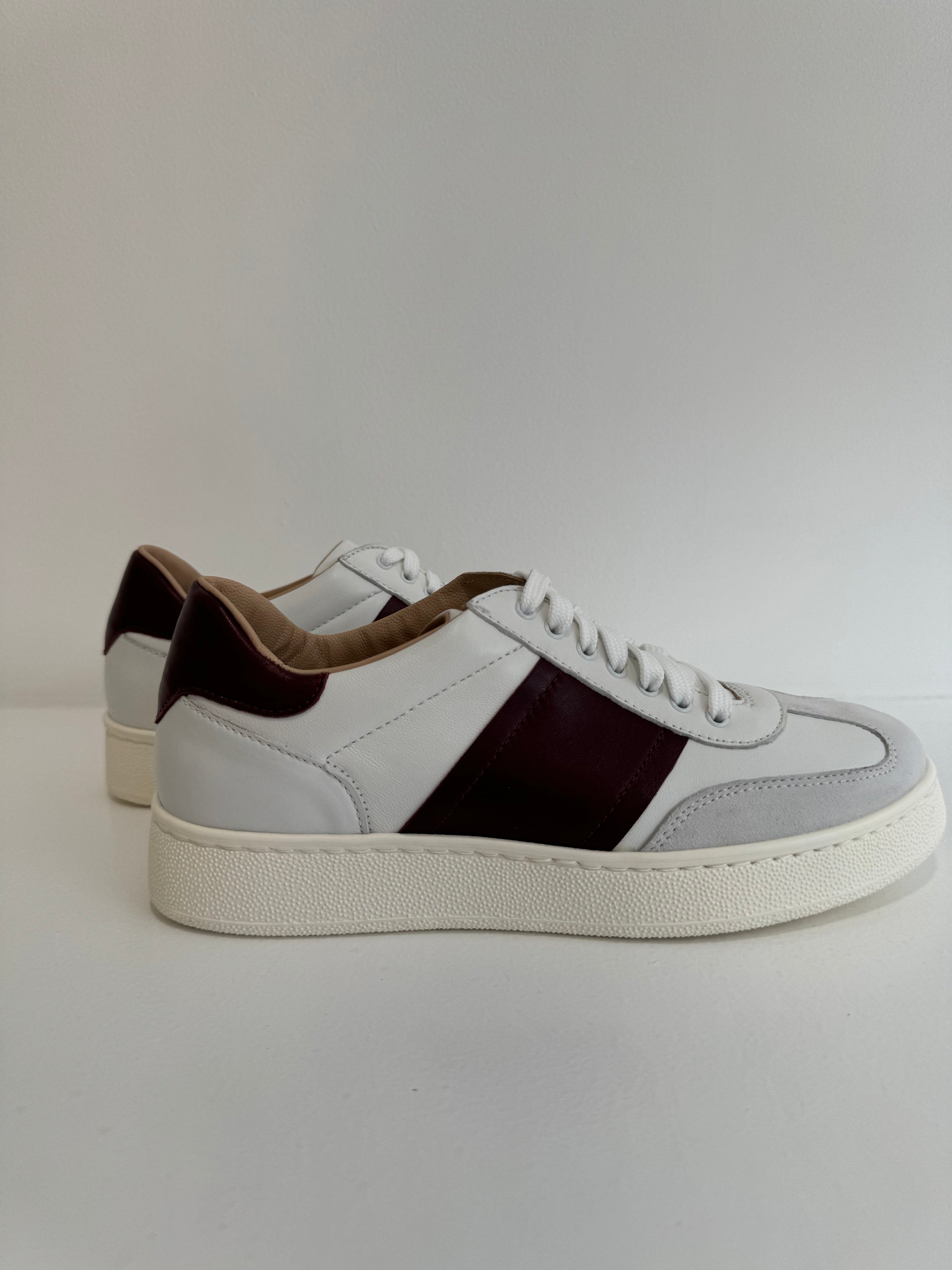 Side view of white leather trainers with bordeaux coloured sidestripe