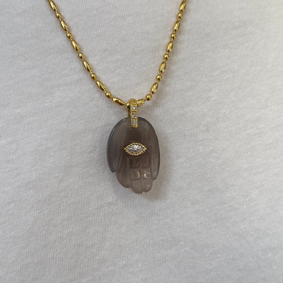close up of grey hand pendant on gold chain necklace on white background 