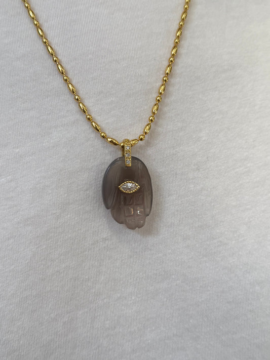 close up of grey hand pendant on gold chain necklace on white background 