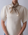 Person wearing a beige blouse with a polka dot scarf on a plain background