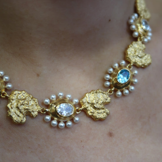 Gold necklace with pearls and blue stones and matching earrings model shot close up