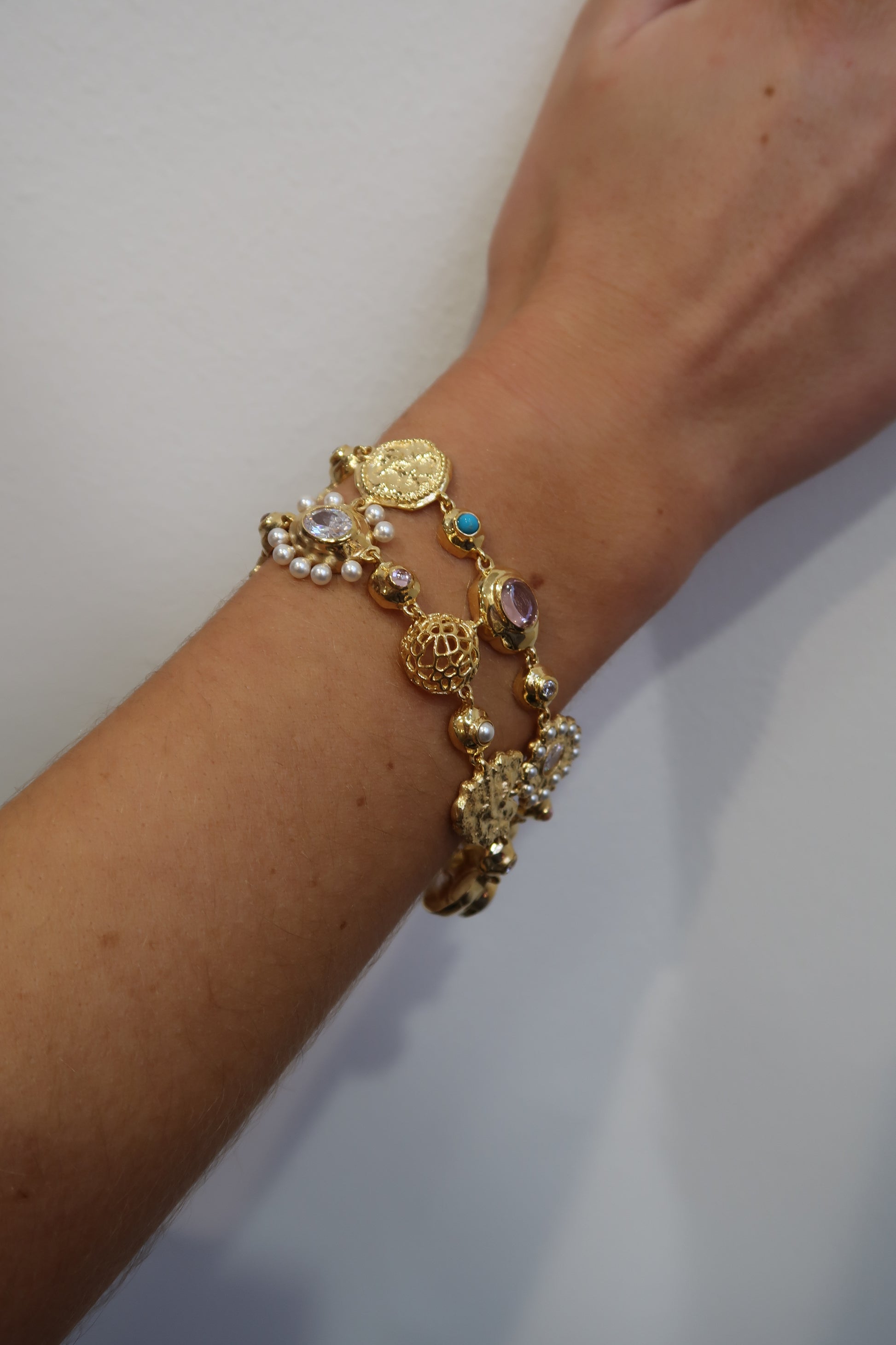 Gold bracelet with blue and pink charms on a wrist against a plain background