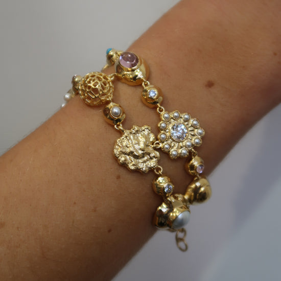 Gold bracelet with blue and pink charms on a wrist against a plain background