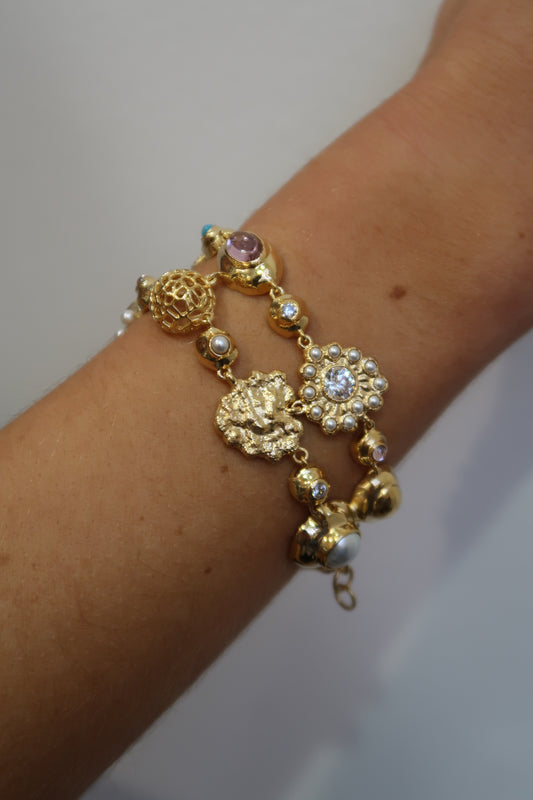Gold bracelet with blue and pink charms on a wrist against a plain background