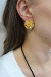 Gold flower earring worn by a person with a black beaded necklace.