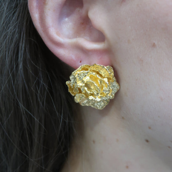 Gold flower earring worn by a person with a black beaded necklace.