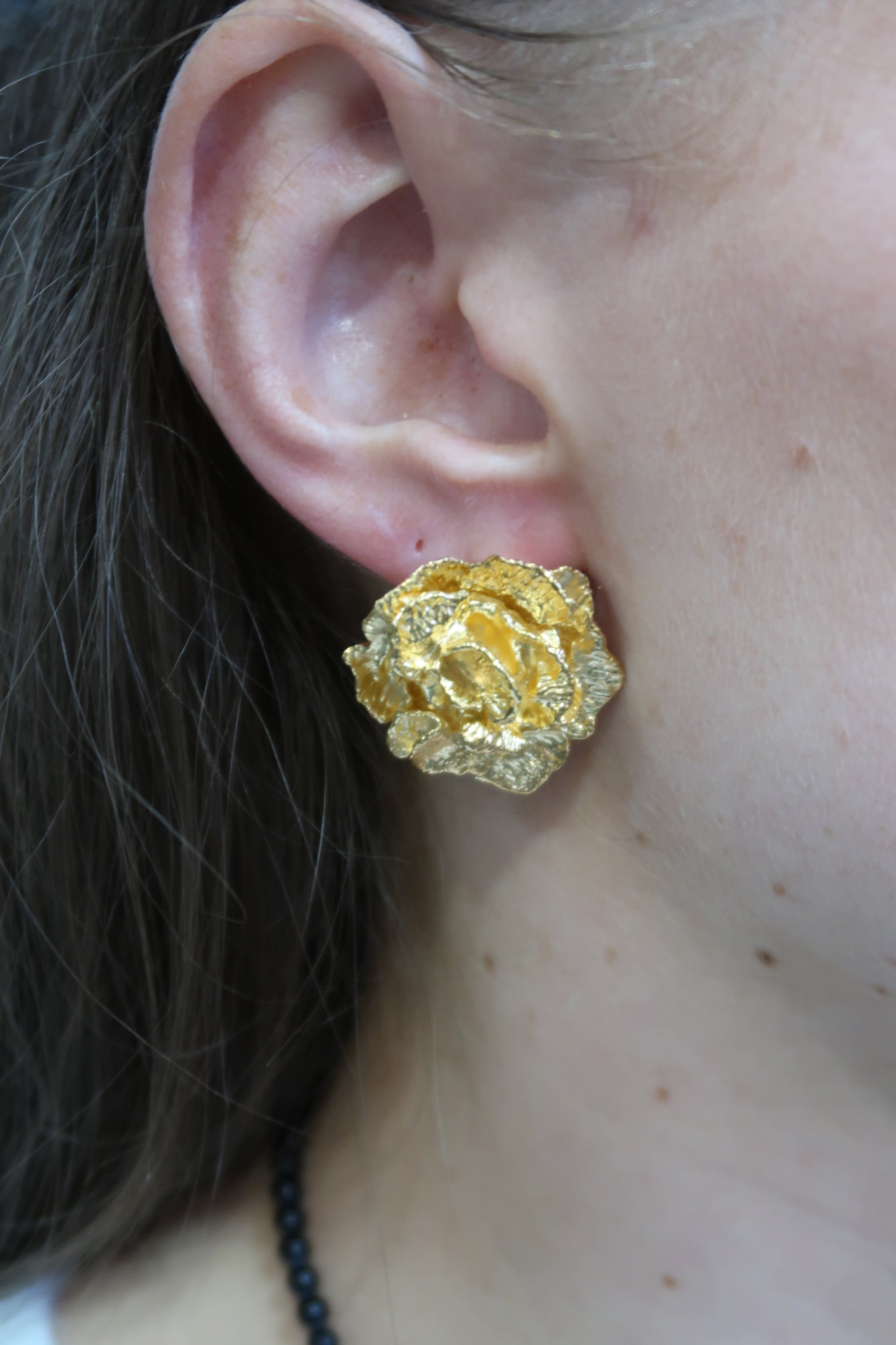 Gold flower earring worn by a person with a black beaded necklace.