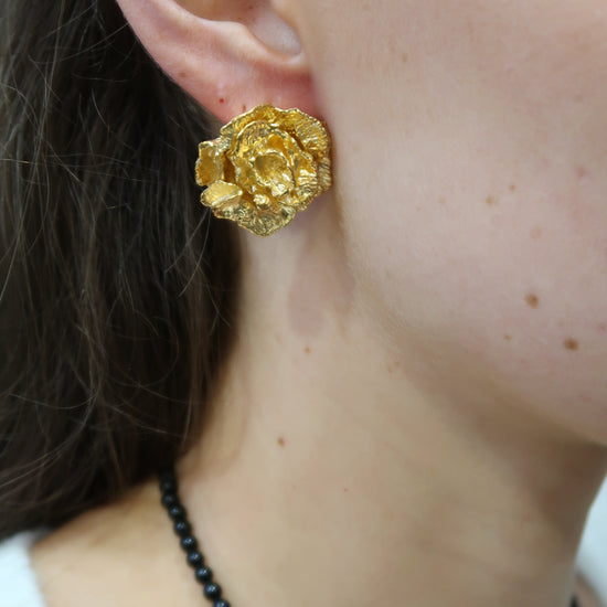 Gold flower earring worn by a person with a black beaded necklace.