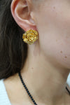 Gold flower earring worn by a person with a black beaded necklace.