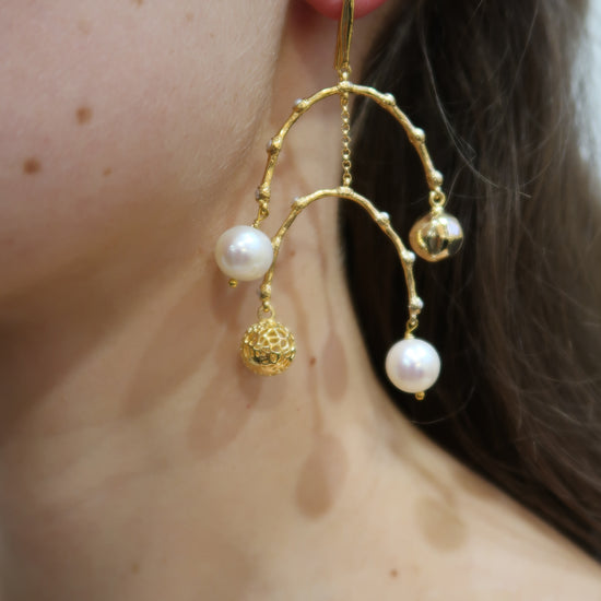 Gold and pearl earring worn on an ear