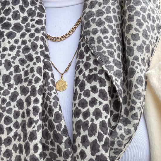 Person wearing a leopard print scarf with a gold necklace and white top.