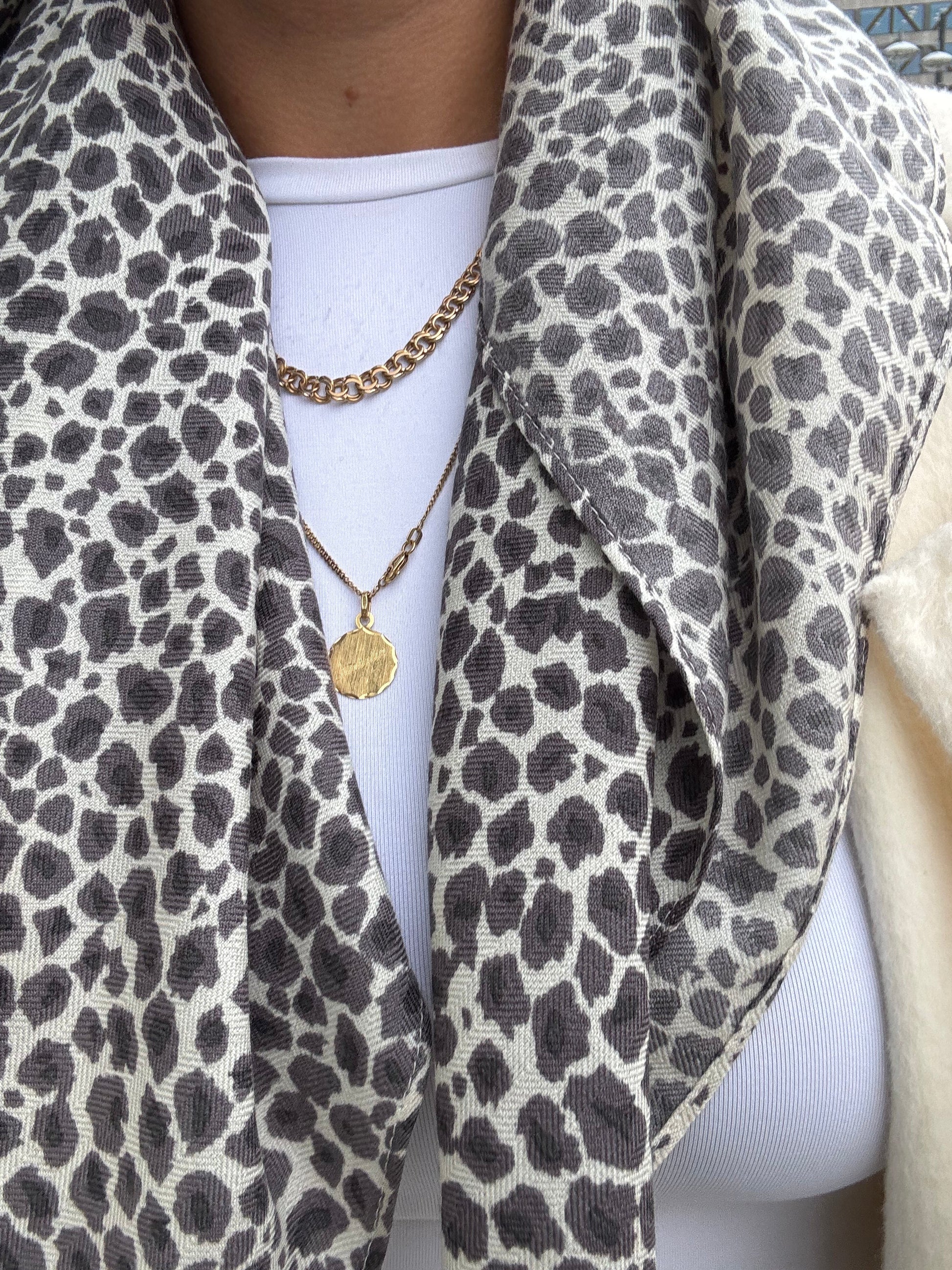 Person wearing a leopard print scarf with a gold necklace and white top.