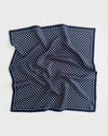 A square navy blue silk scarf with a white polka dot pattern and a dotted border, laid flat on a light gray background.