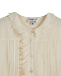 Cream button through top with ruffle details and short puff sleeves with ruffle cuffs and pin tuck details at the front of the bodice with peter pan collar and scalloped edge