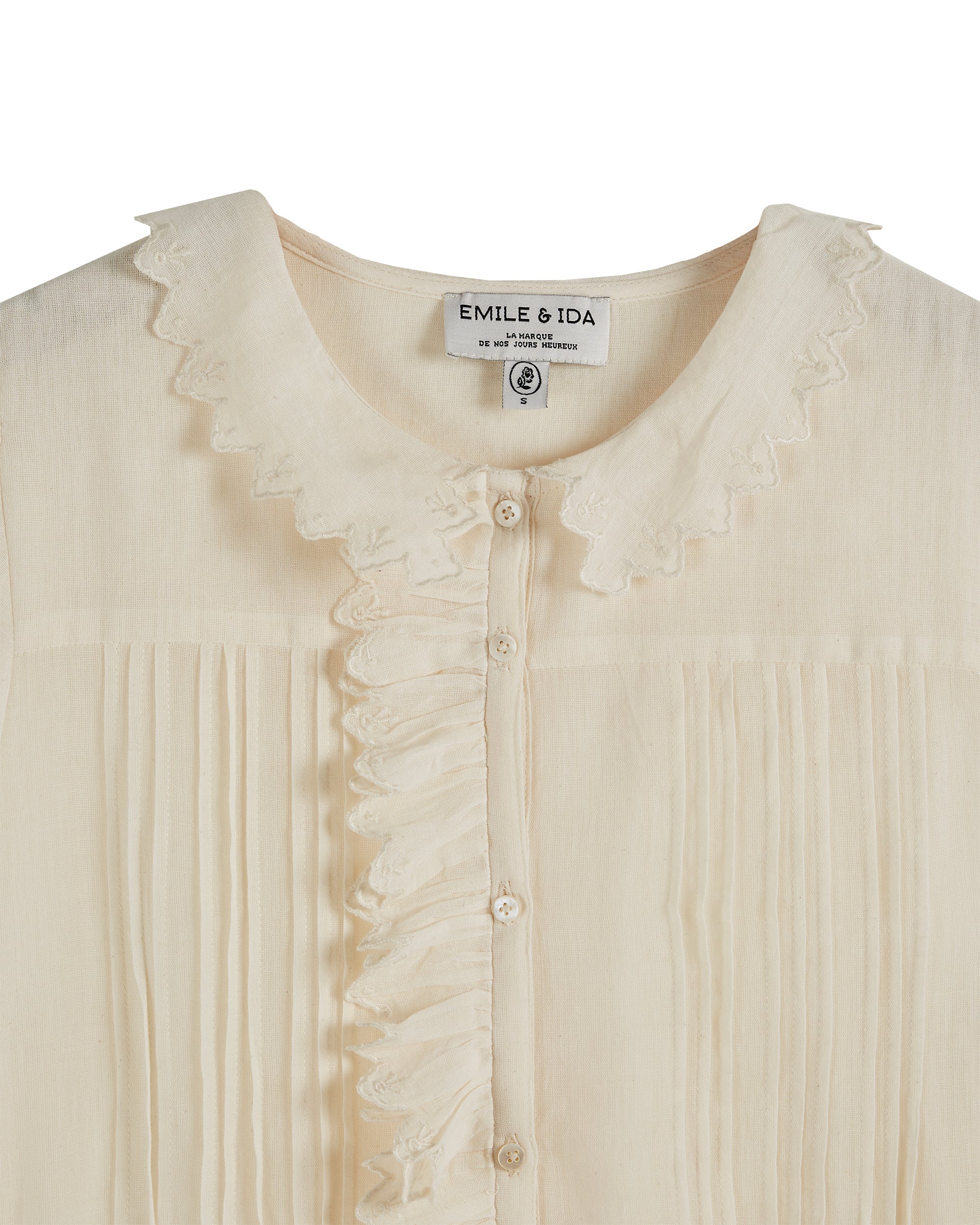 Cream button through top with ruffle details and short puff sleeves with ruffle cuffs and pin tuck details at the front of the bodice with peter pan collar and scalloped edge