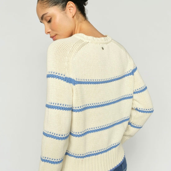 Woman wearing a cream sweater with blue stripes on a plain background