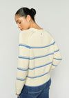 Woman wearing a cream sweater with blue stripes on a plain background