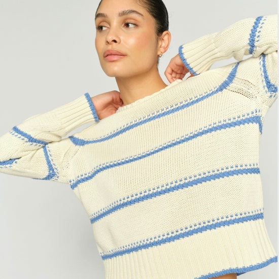 Woman wearing a cream and blue striped sweater against a light gray background