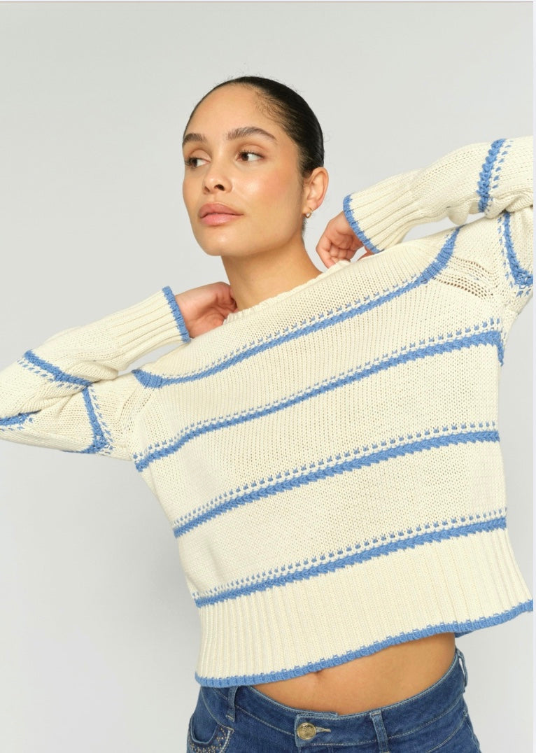 Woman wearing a cream and blue striped sweater against a light gray background