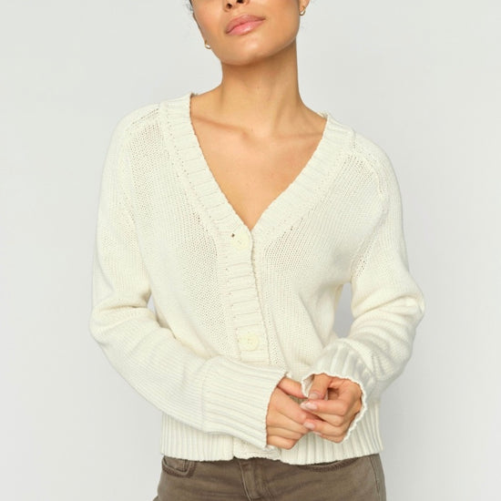 Woman wearing a cream cardigan and brown pants against a white background