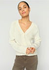 Woman wearing a cream cardigan and brown pants against a white background