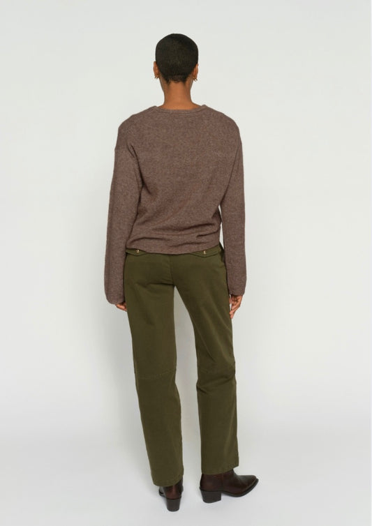 Person wearing a brown sweater and green pants on a white background