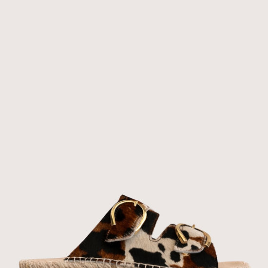 Cow print sandal with gold buckles and a woven sole 