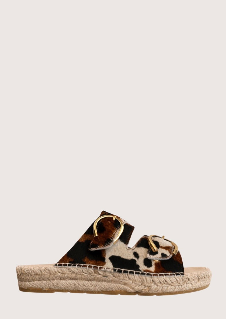 Cow print sandal with gold buckles and a woven sole 