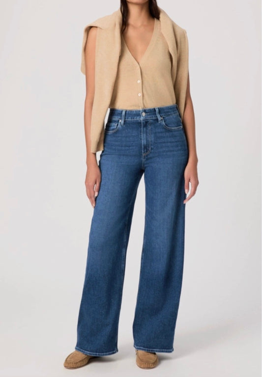 Person wearing a beige cardigan, beige top, and blue jeans on a white background