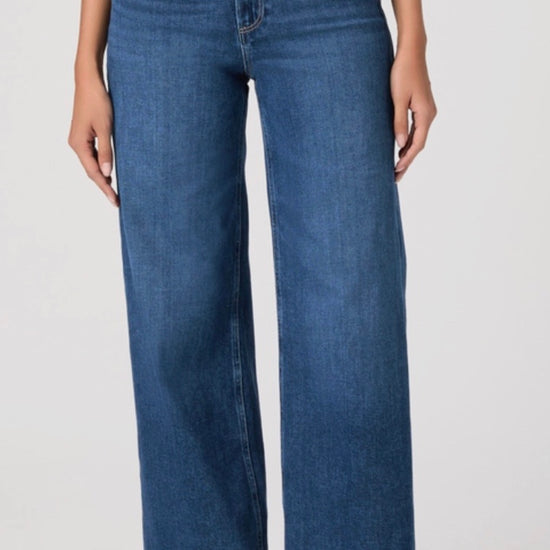 Person wearing a beige cardigan, beige top, and blue jeans on a white background