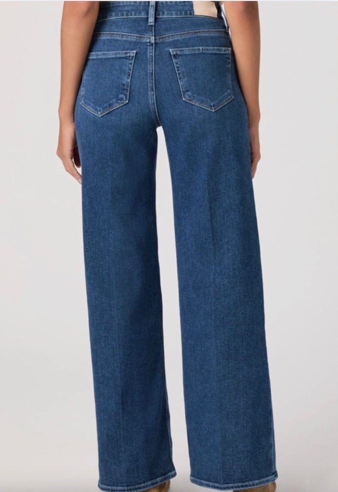 Person wearing a beige cardigan, beige top, and blue jeans on a white background