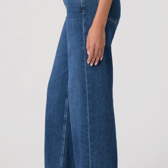 Person wearing a beige cardigan, beige top, and blue jeans on a white background