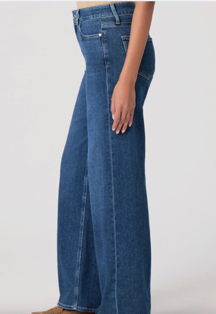 Person wearing a beige cardigan, beige top, and blue jeans on a white background