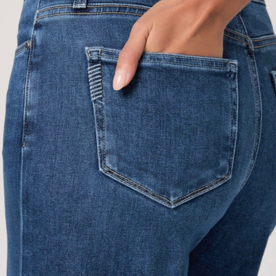 Person wearing a beige cardigan, beige top, and blue jeans on a white background