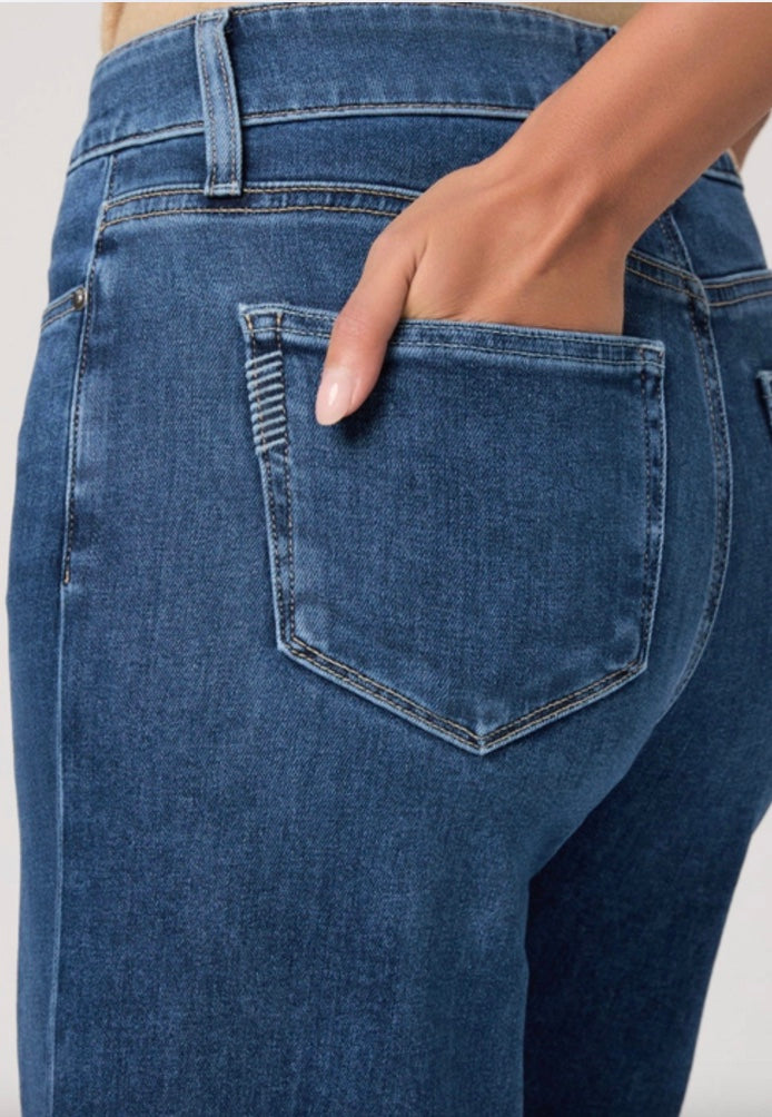 Person wearing a beige cardigan, beige top, and blue jeans on a white background
