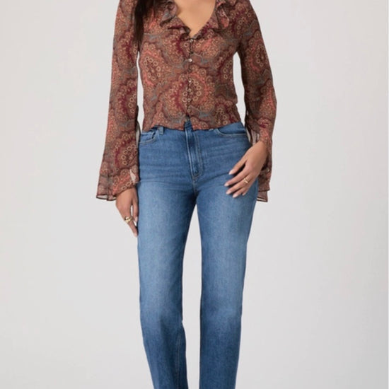 Woman wearing a patterned blouse and blue jeans on a white background