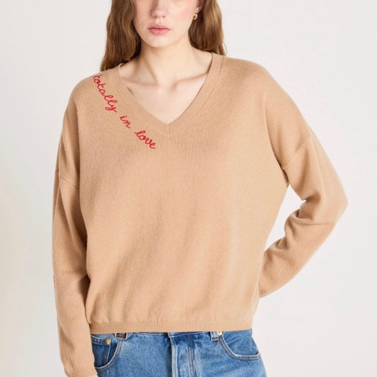 Woman wearing a beige sweater with text and blue jeans on a white background