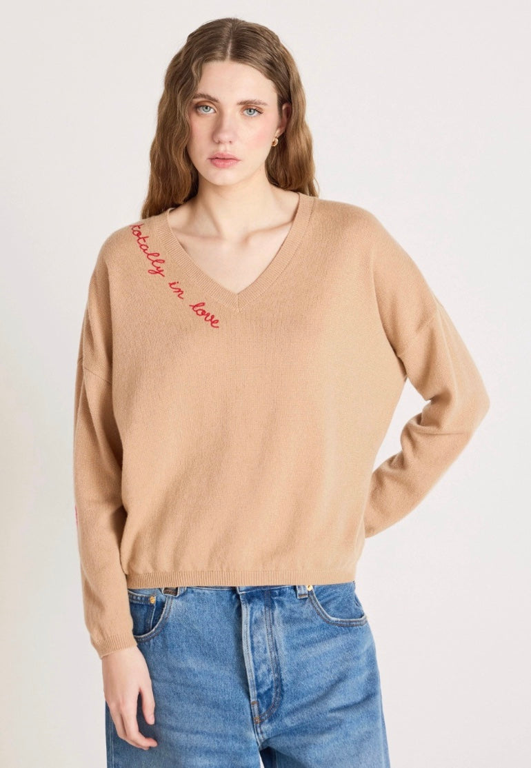Woman wearing a beige sweater with text and blue jeans on a white background