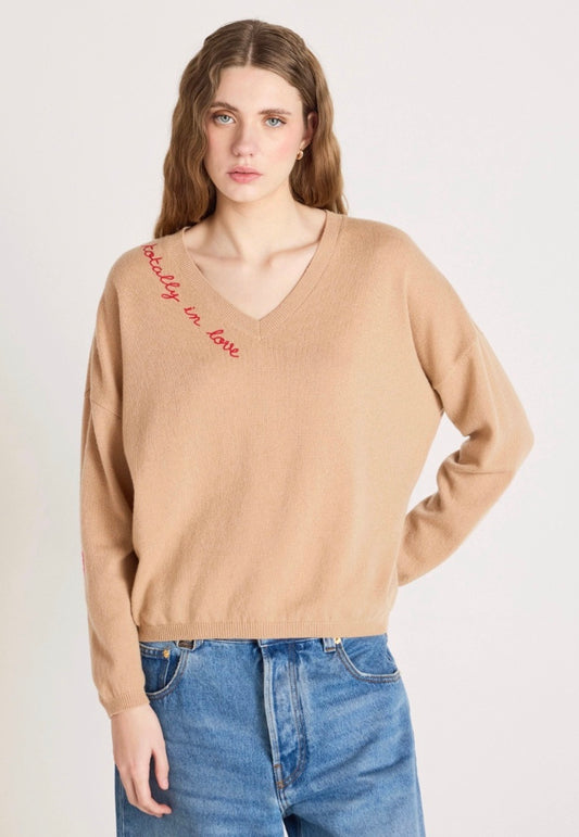 Woman wearing a beige sweater with text and blue jeans on a white background